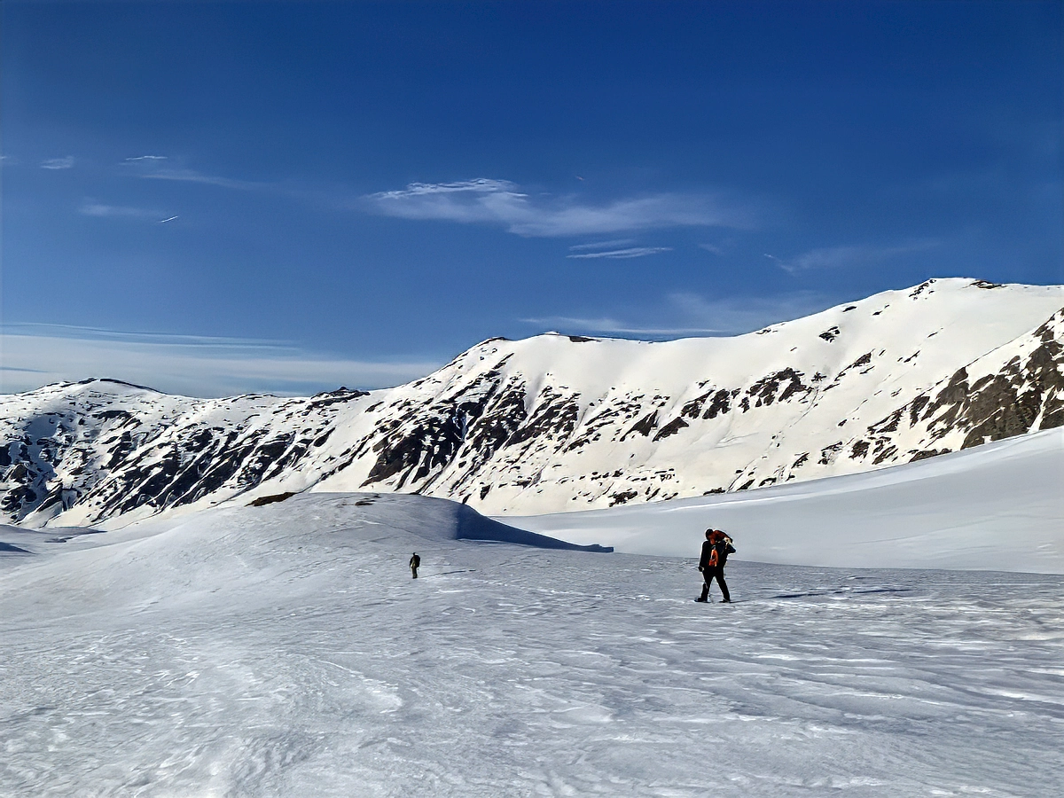 Two tiny figures crossing a vast open snow plateau
