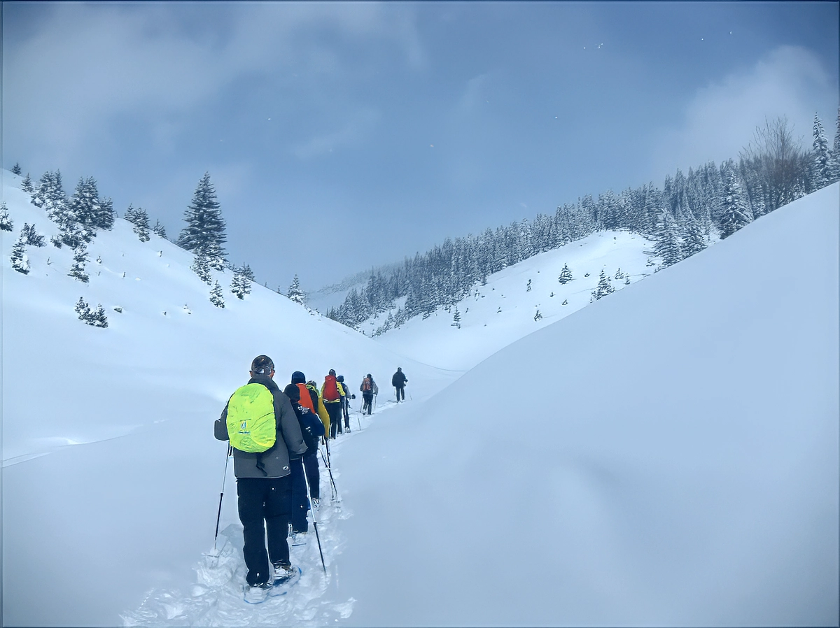 A guided group moving in single file through deep snow on a mountain slope