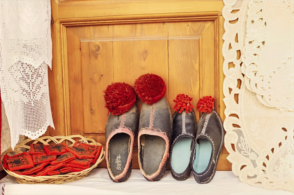 Traditional Albanian felt shoes with red pom-poms beside lace and embroidery