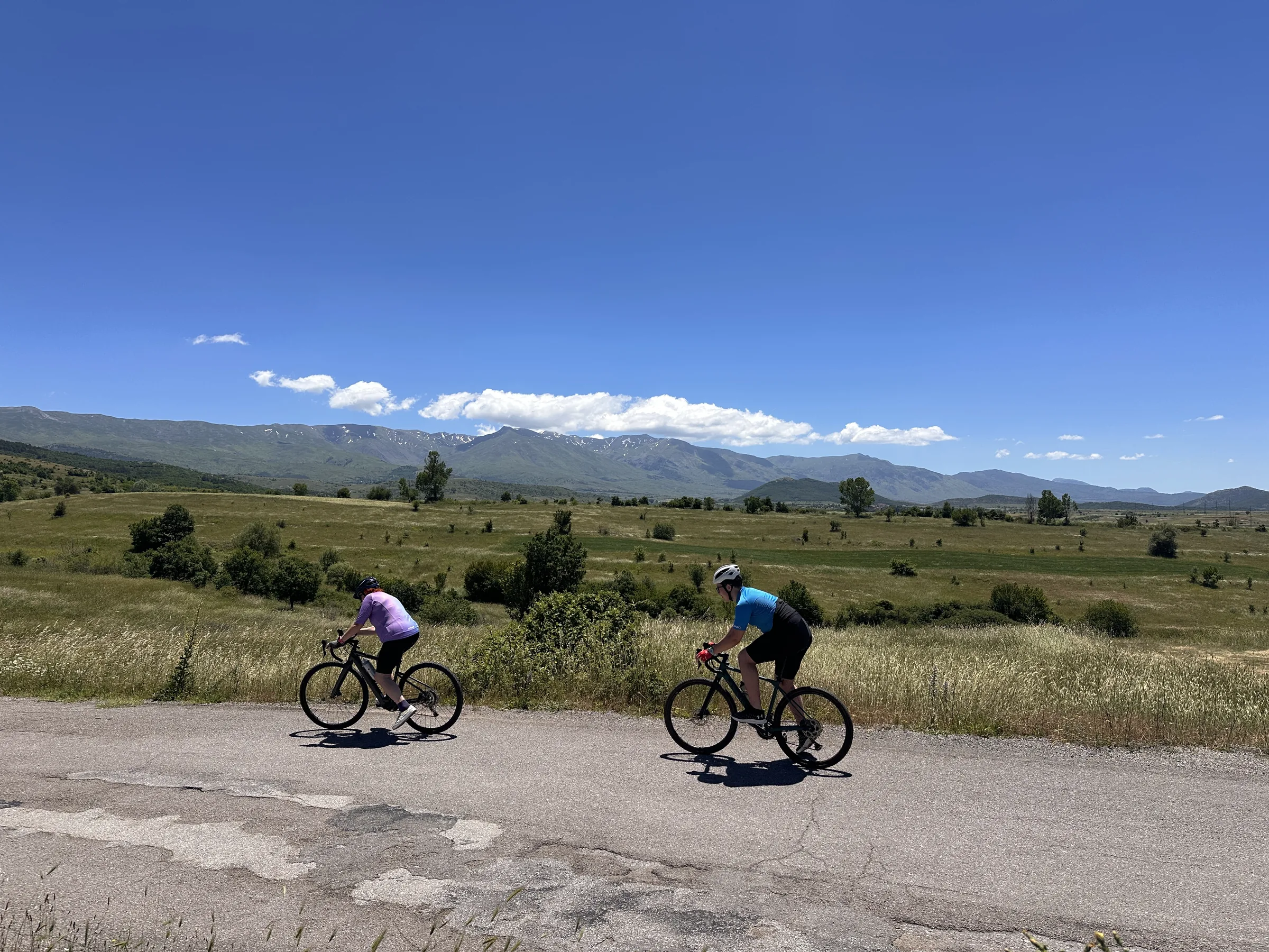 Two cyclists on an open road across a wide plain below mountains