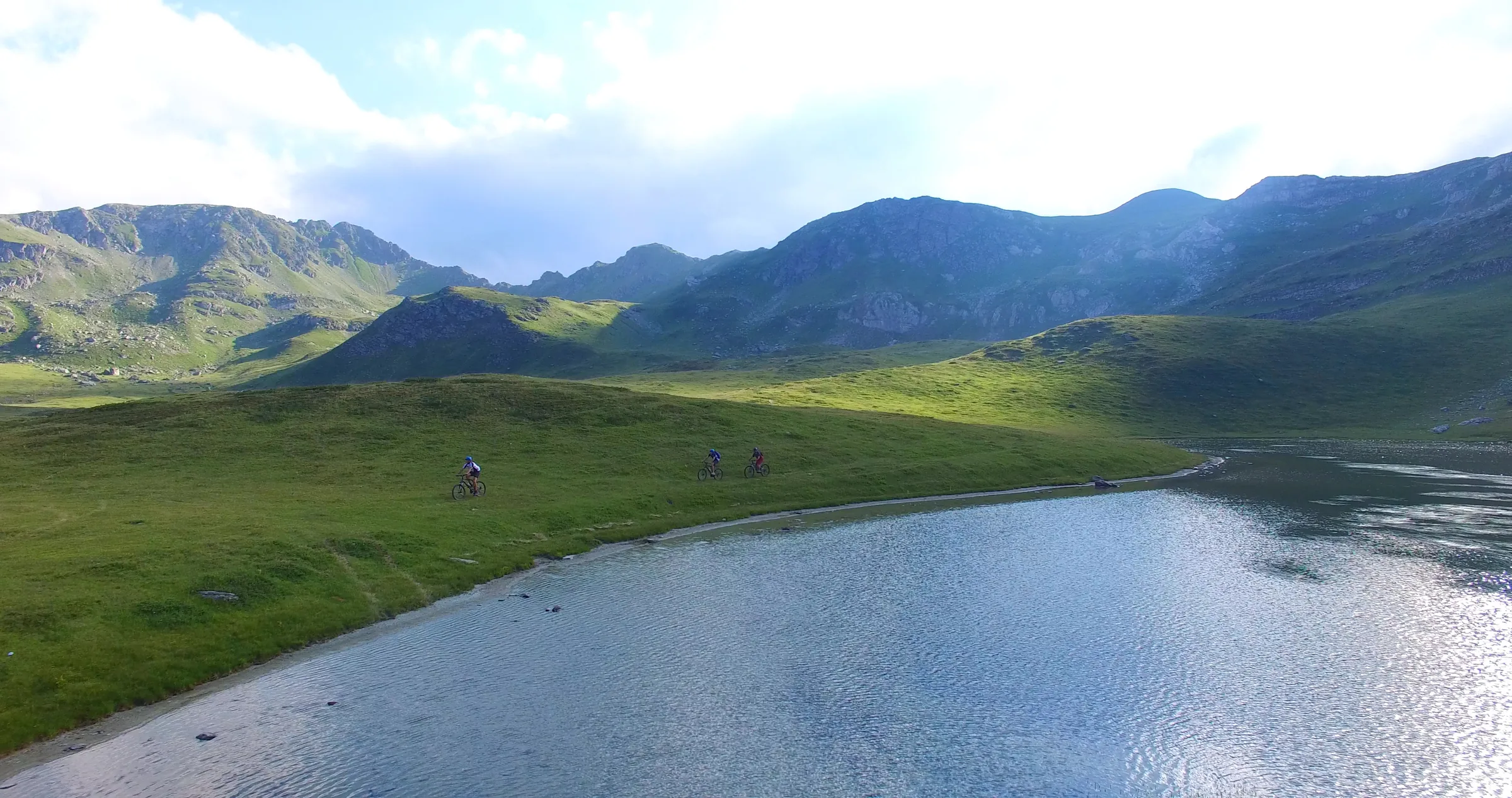 Three cyclists riding along the shore of a mountain lake
