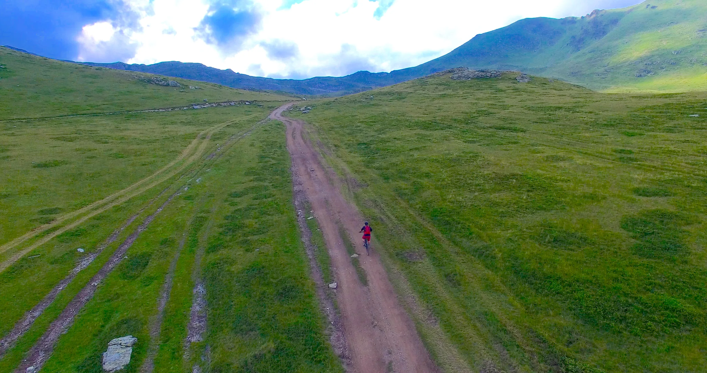 Aerial view of a cyclist alone on a track across high green pasture