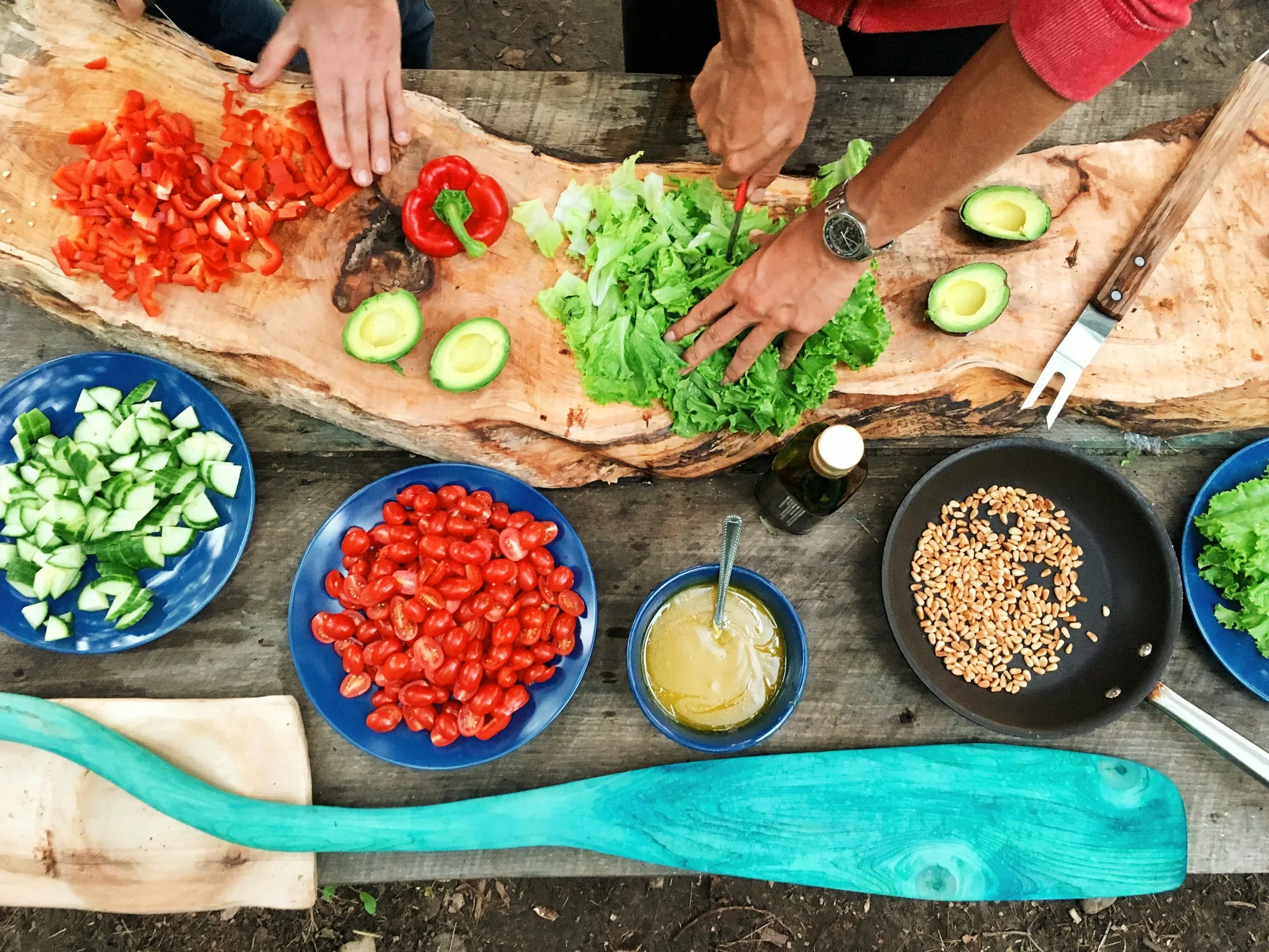 A long table of fresh vegetables and salads being prepared outdoors