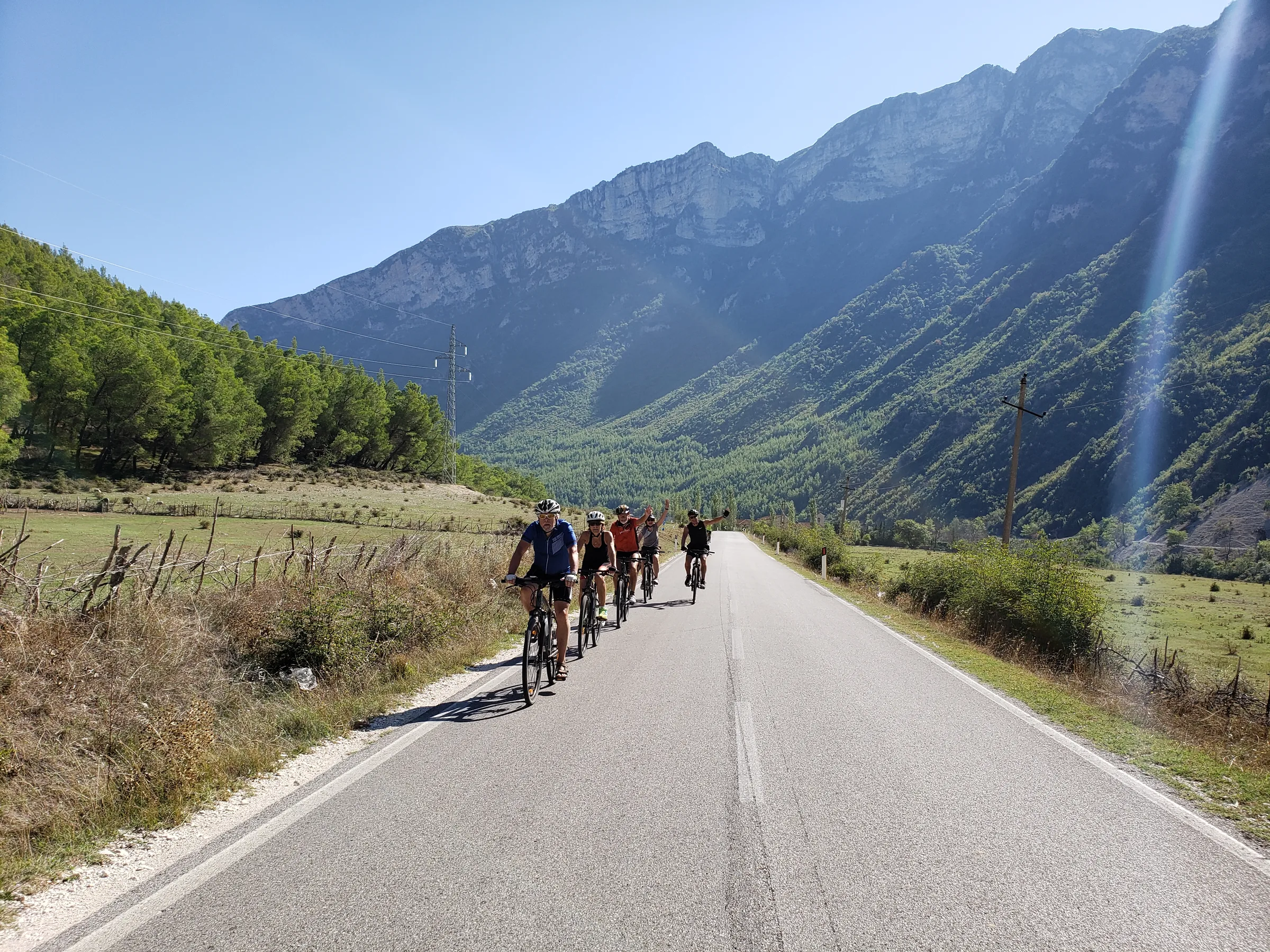 A group of cyclists riding together on a quiet road below mountains