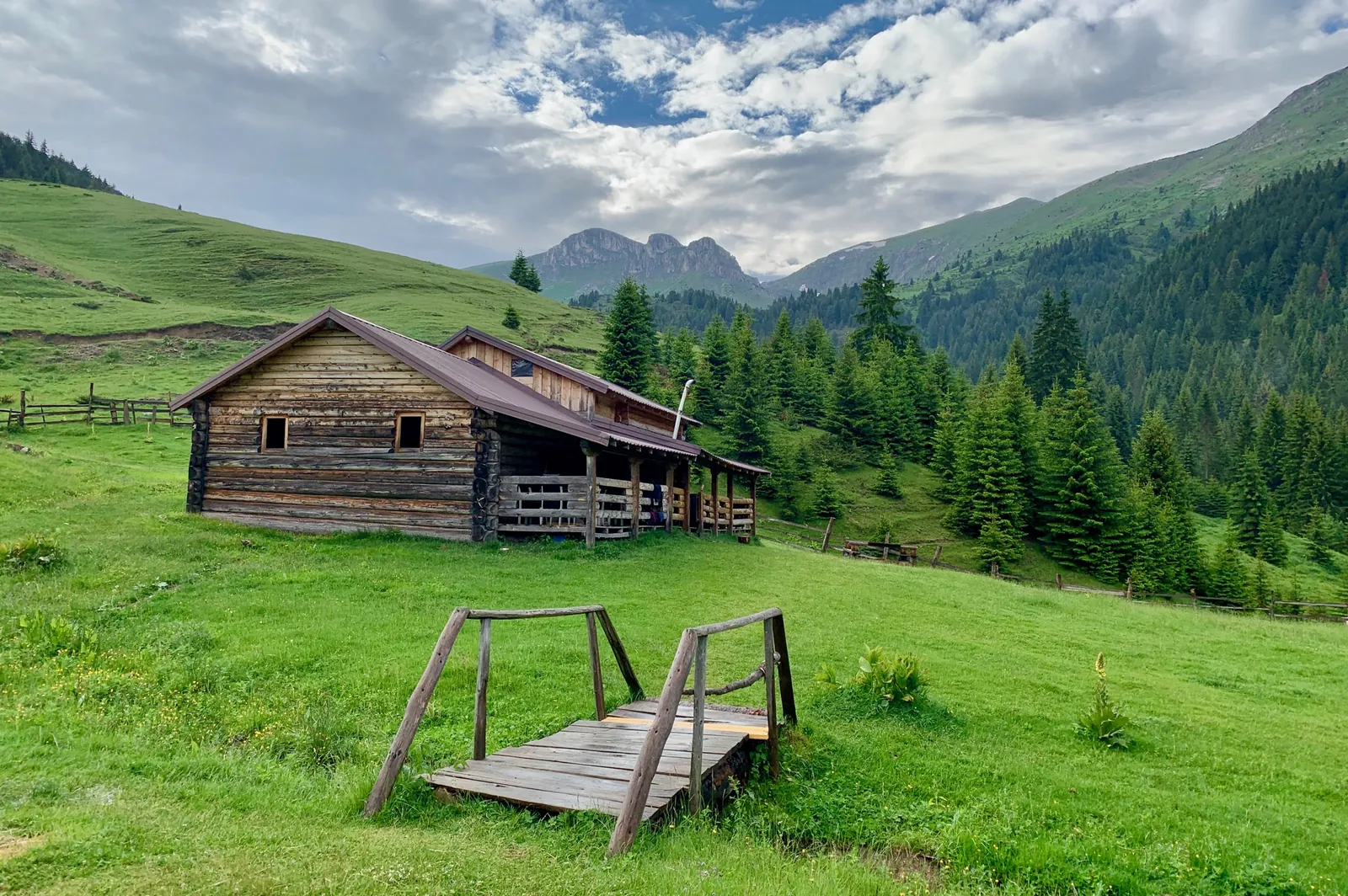 A timber mountain hut and log bridge on a green Albanian pasture
