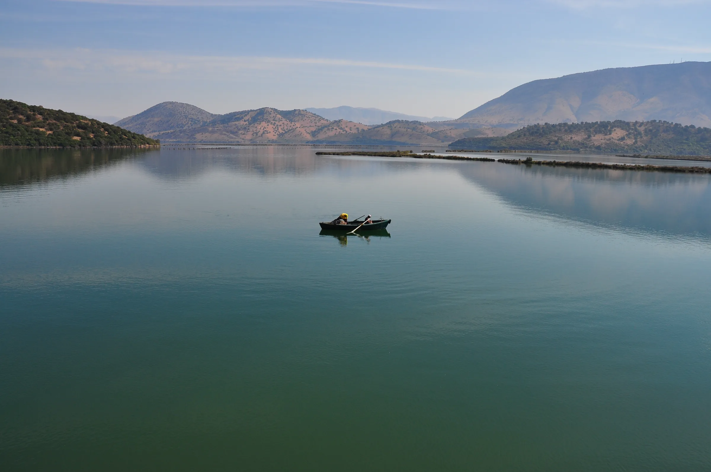 A small rowing boat alone on wide still water between low hills