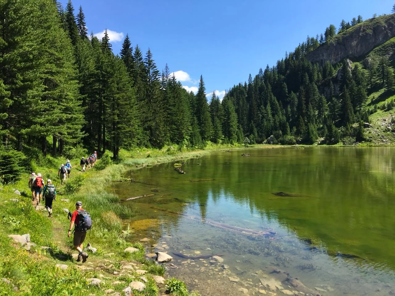 A line of walkers following the shore of a clear mountain lake