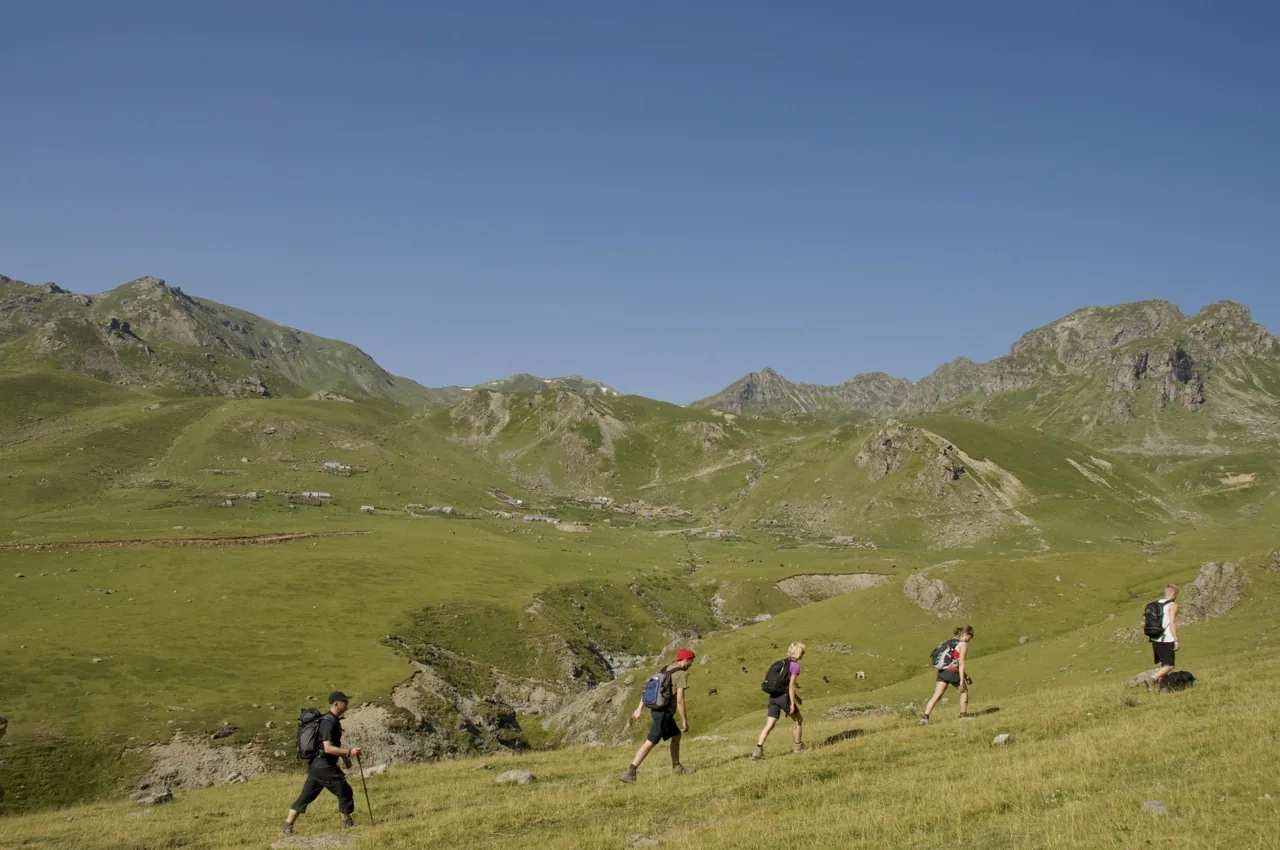 Walkers crossing open summer pastures below rocky peaks